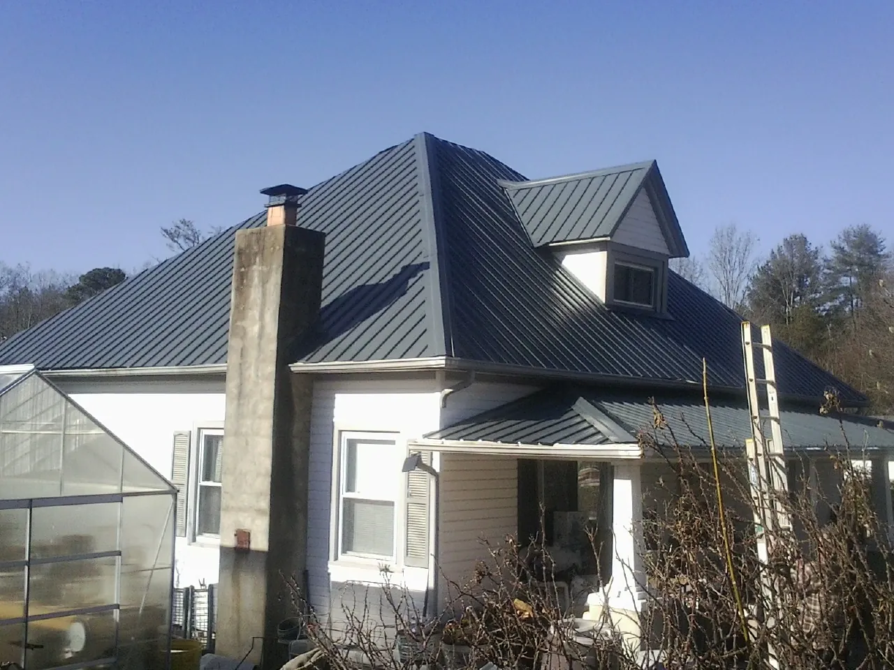 Dark blue standing seam metal roof on a white farmhouse with dormer — Slate & Tile Roof Repair by Roofing Brothers in Brown City