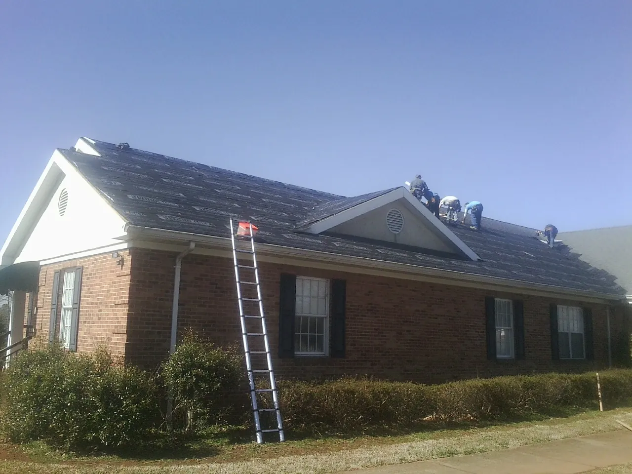 Crew tearing shingles off a brick ranch roof with a ladder set — Emergency Roof Repair work by our crew in Brown City