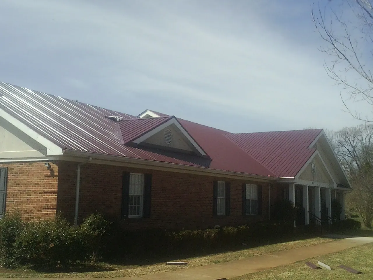 Red metal roof with gabled entries on a long brick building, from a Hail Damage Roof Repair job in Brown City