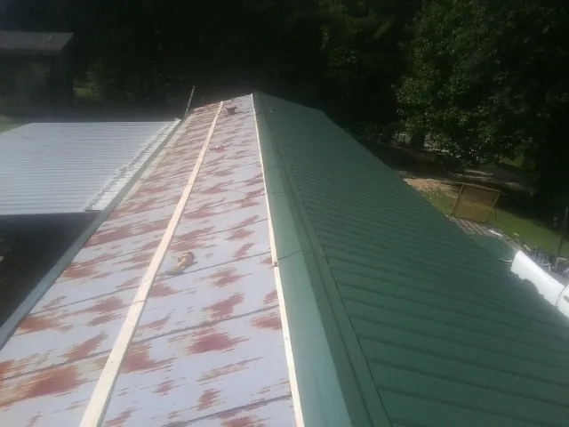 Old rusted panels beside newly installed green metal roofing — Wind Damage Roof Repair by Roofing Brothers in Brown City