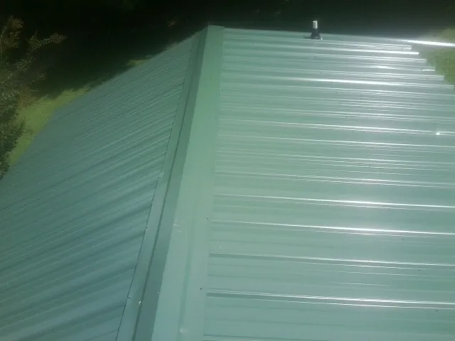 New green metal panels meeting at the ridge of a roof — Flat Roof Repair work by our crew in Brown City