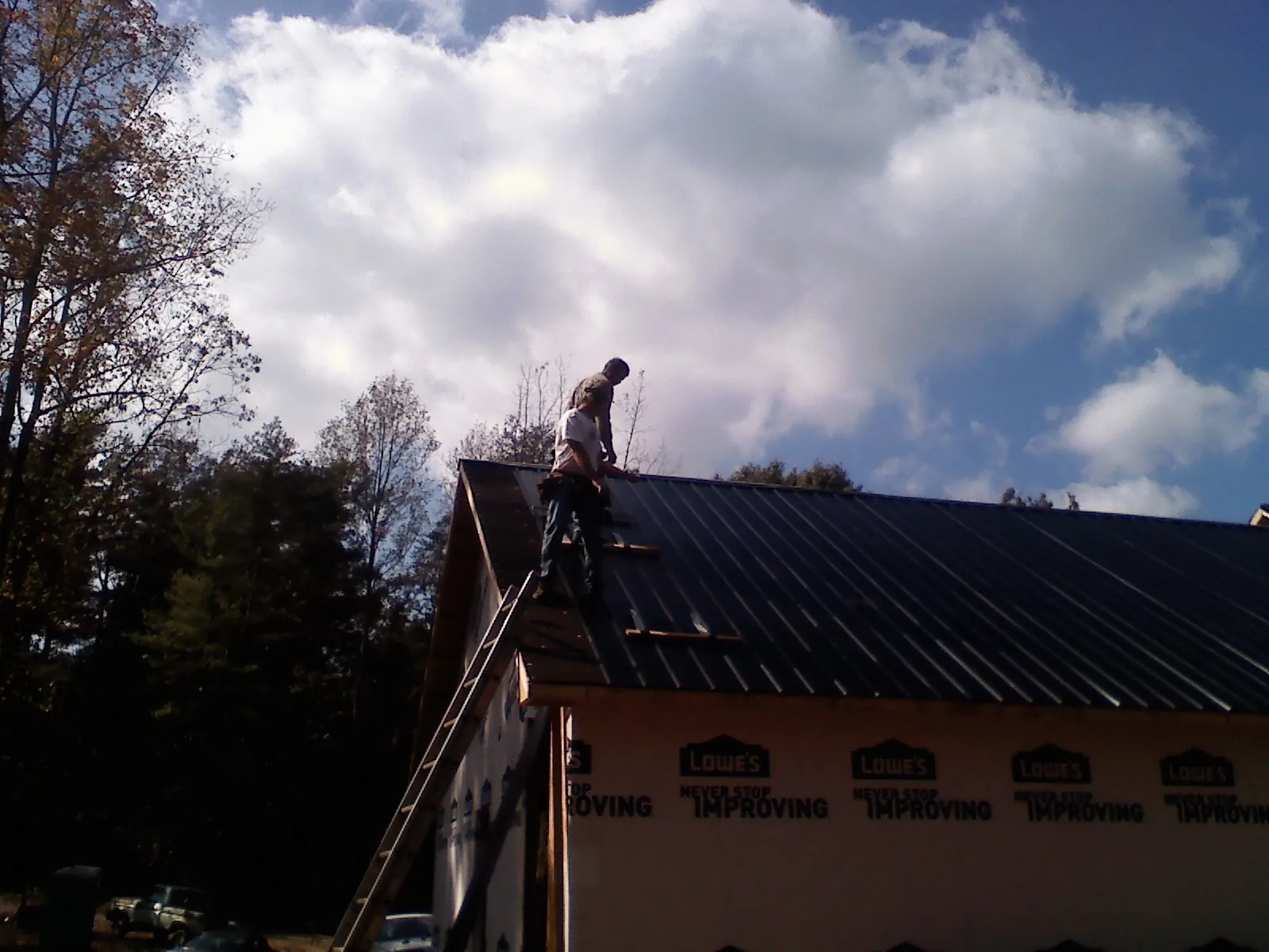 Roofer fastening dark metal panels high against a cloudy sky, from a Roof Inspection job in Brown City