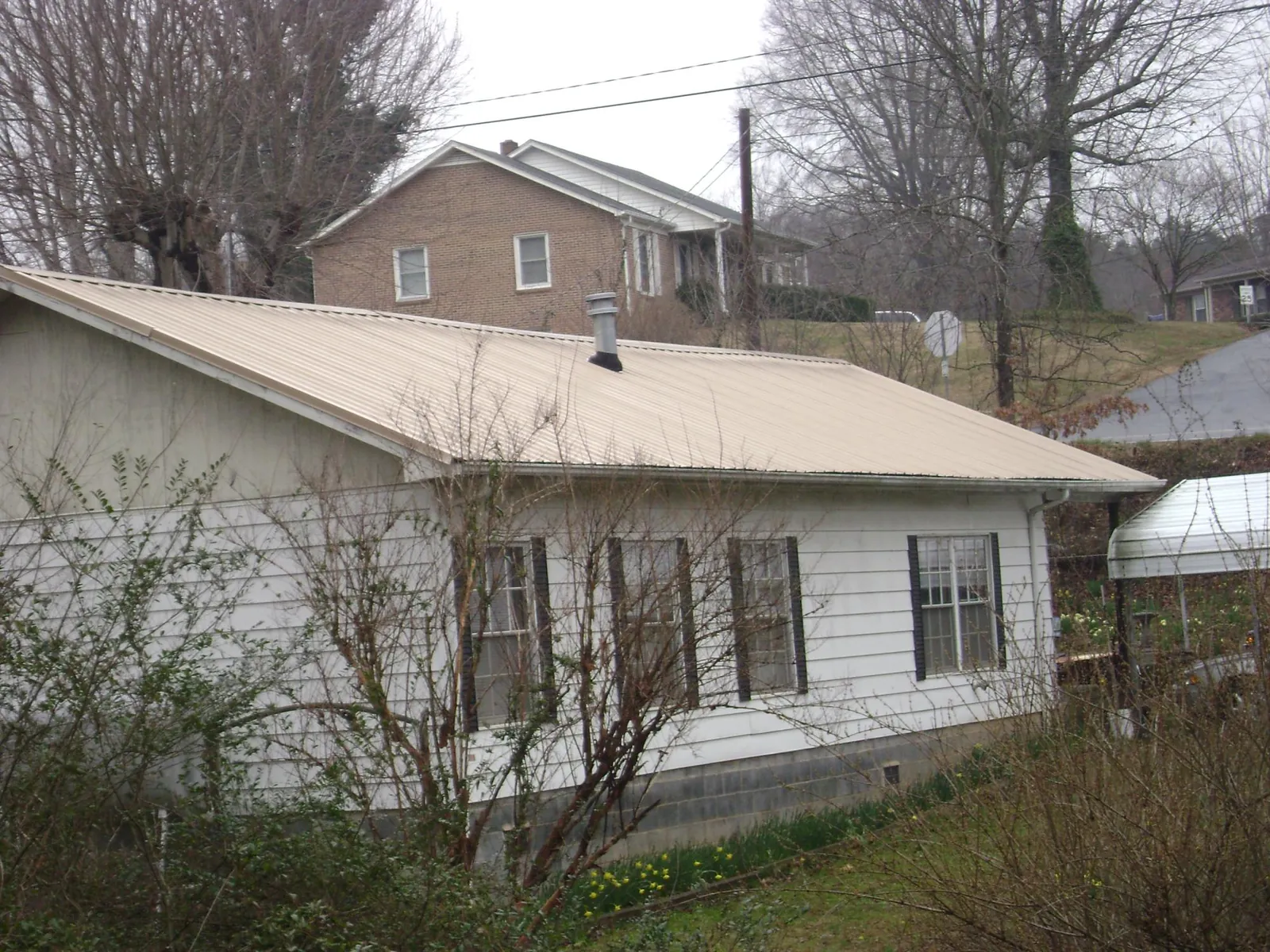 Tan metal roof on a white sided house set into a hillside — Commercial Roofing by Roofing Brothers in Brown City