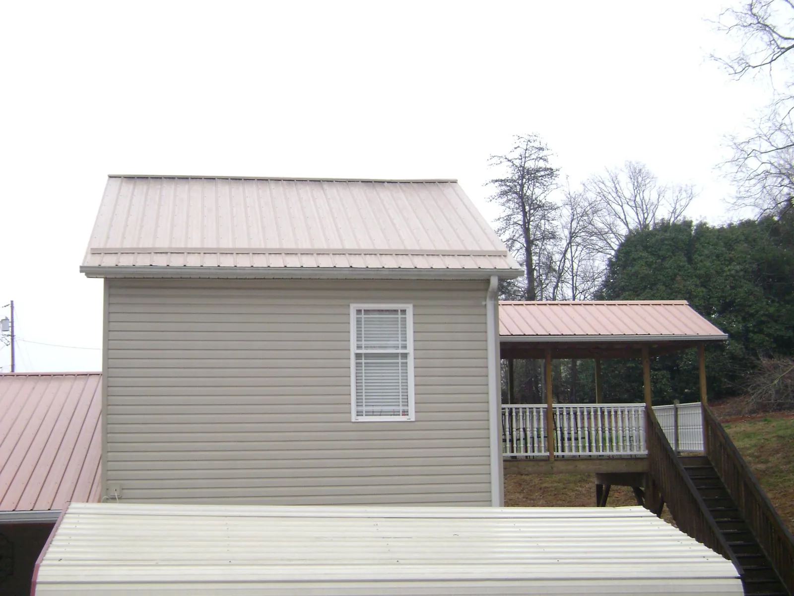 Tan metal roofs on a two story addition and attached porch, from a Roof Replacement job in Brown City